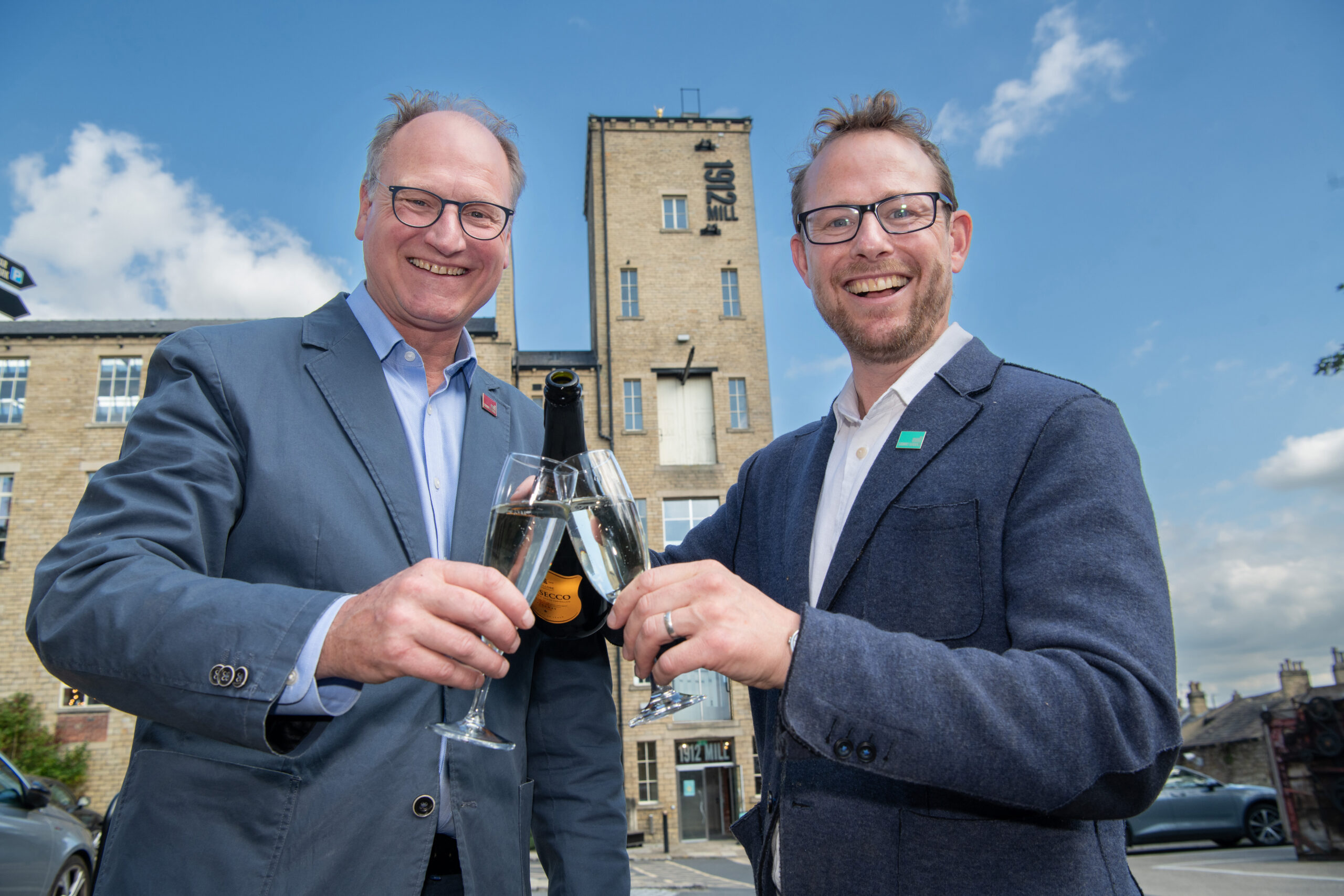 William and John Gaunt in front of the 1912 Mill with two champagne glasses being filled