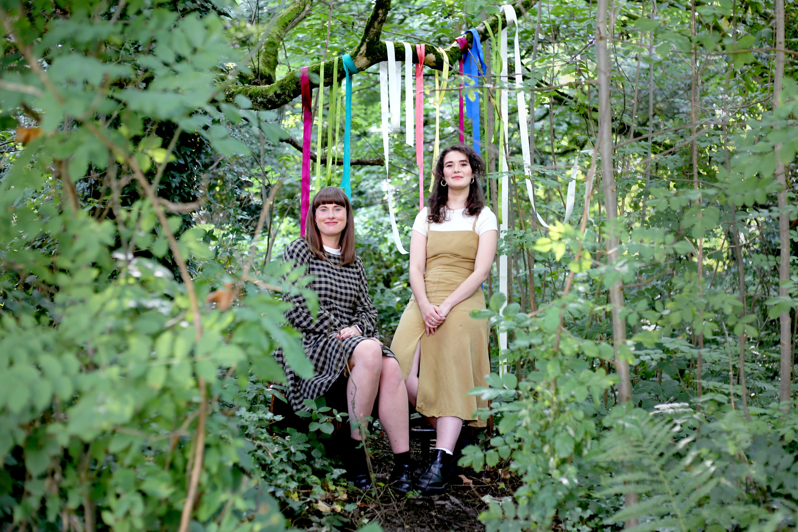 2 women sat in woodland with ribbons around them
